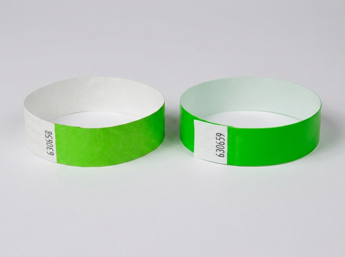 Sammenligning side om side af et hvidt Tyvek-armbånd med trykt stregkode og et farvet identifikationsarmbånd med stregkode, placeret på et festivalbord
